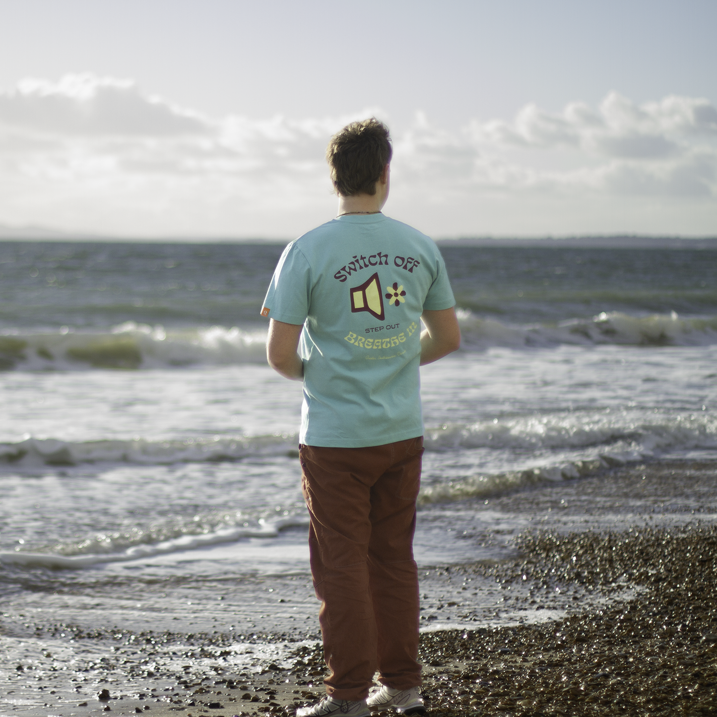 Person wearing QUIETER Switch Off tee in retro reef, back view with sea in background