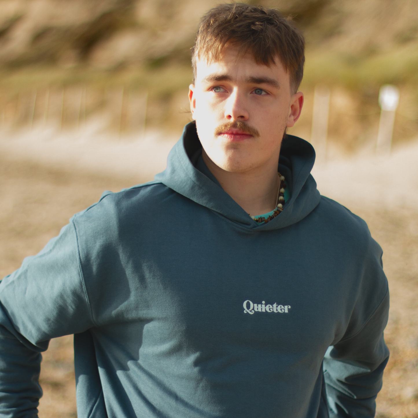 Man wearing a blue hoodie with 'Quieter' logo outdoors