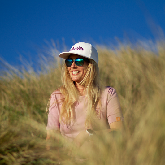Woman wearing a white cap and sunglasses sitting in tall grass with a blue sky background