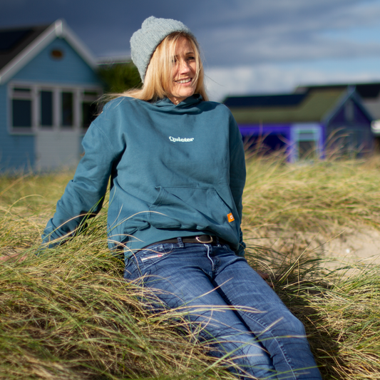 Person wearing a blue hoodie and jeans sitting in tall grass with houses in the background