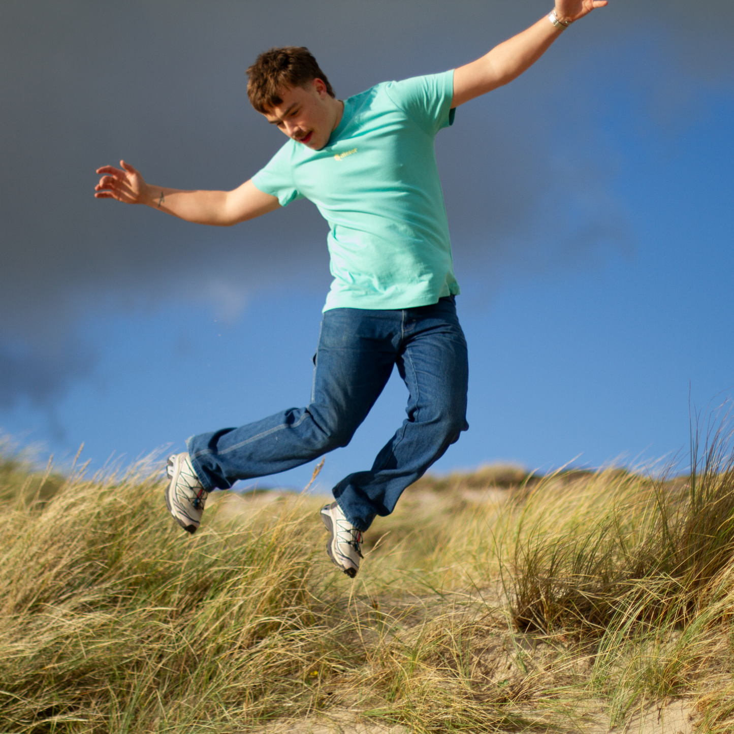 Person jumping outdoors wearing a QUIETER Switch Off tee in retro reef