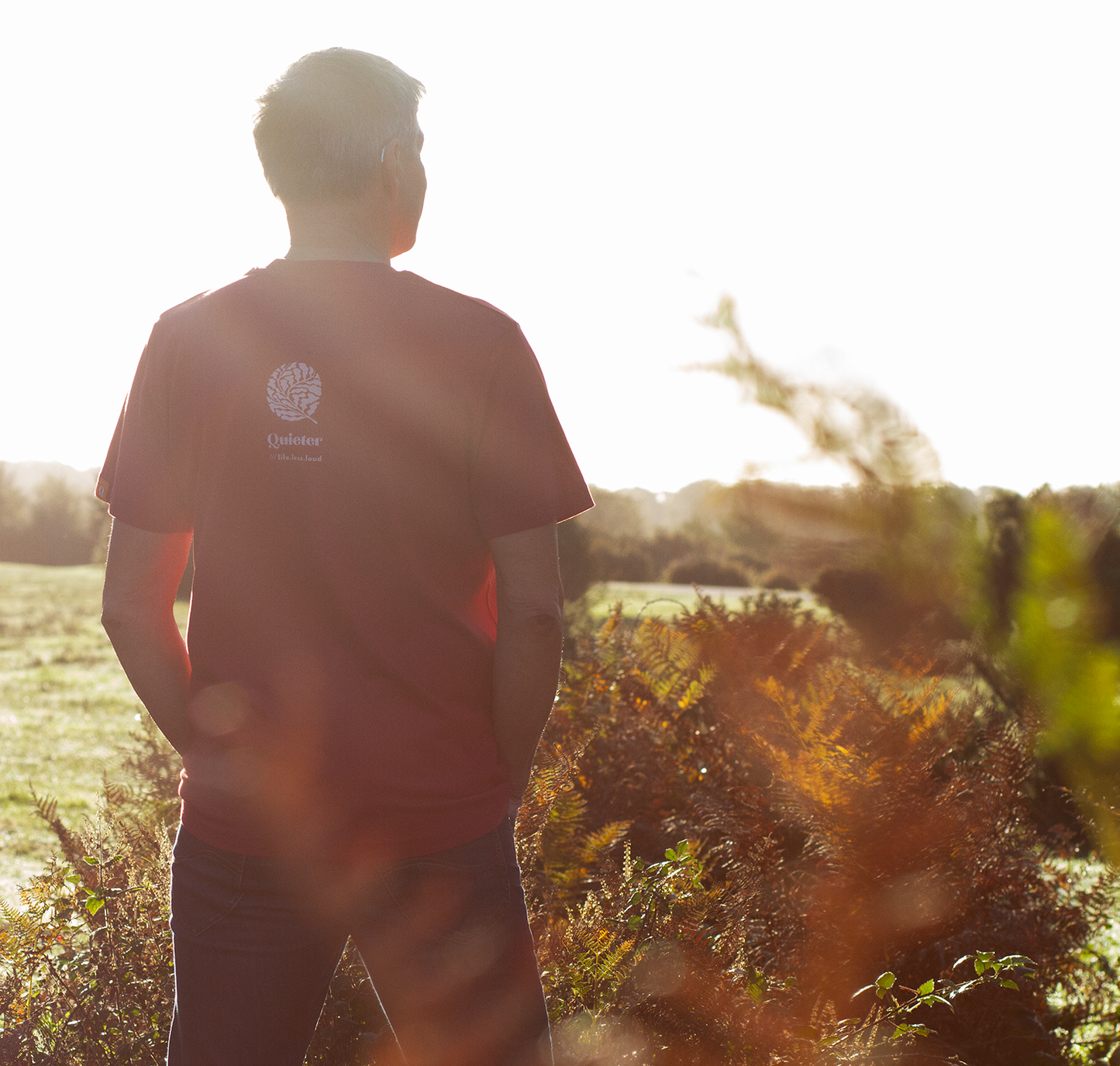 Person wearing QUIETER Squeeze More Trees dust red tee, back view in natural light