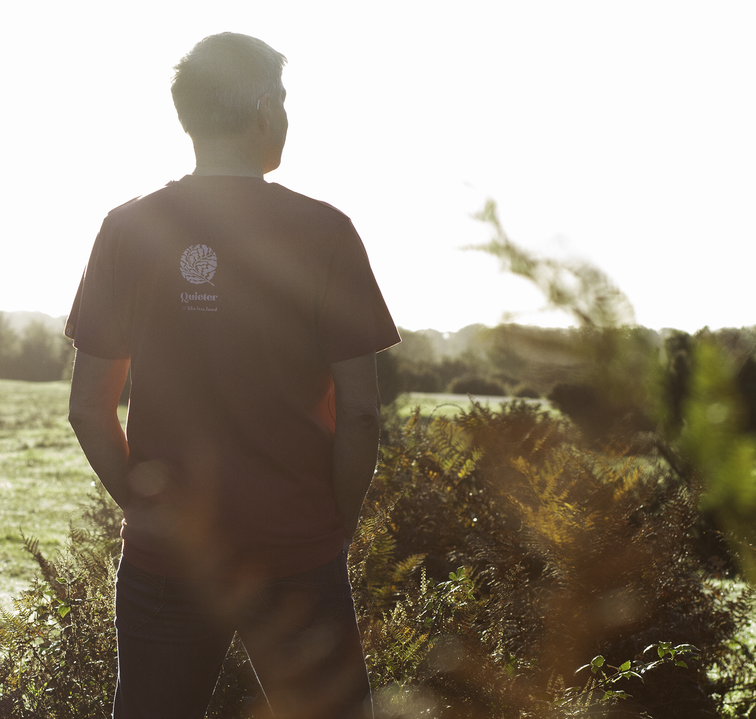 Person wearing QUIETER Squeeze More Trees dust red tee, back view in natural light