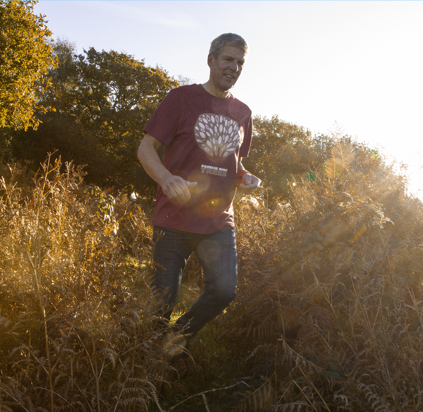 Person running outdoors wearing a QUIETER Squeeze More Trees tee in dust red